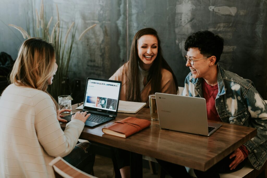 A group of three people sitting at a table with their laptops open and laughing in a cozy setting | Rossera user experience