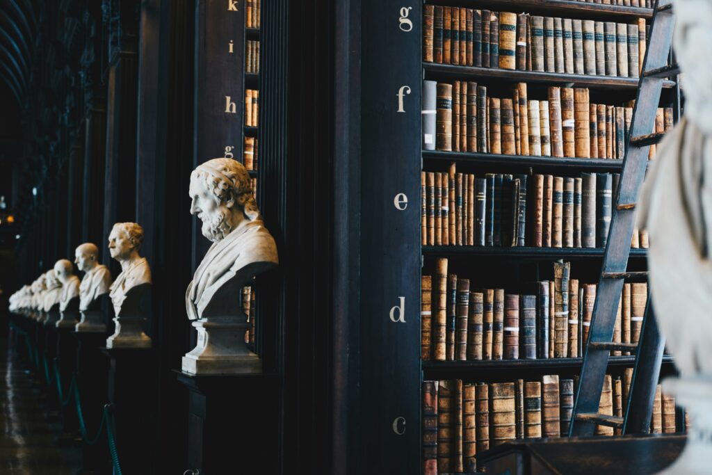 library with books on rows of black wooden shelves and sculpture busts in front of them