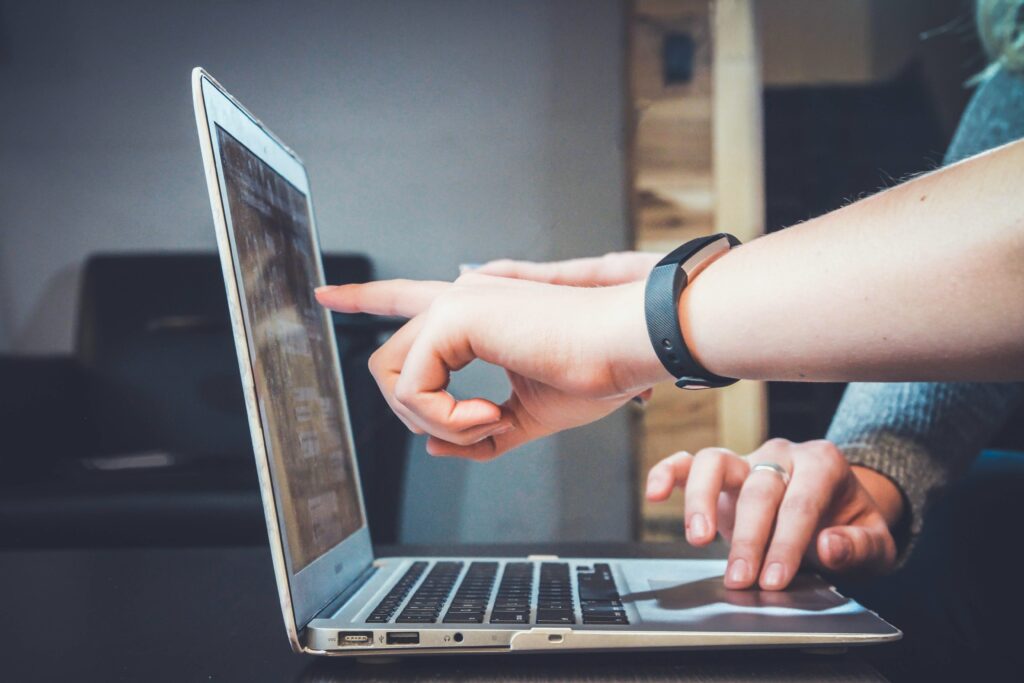 Two hands pointing at a laptop screen while one more plays with the mousepad | Unit4 non-profit