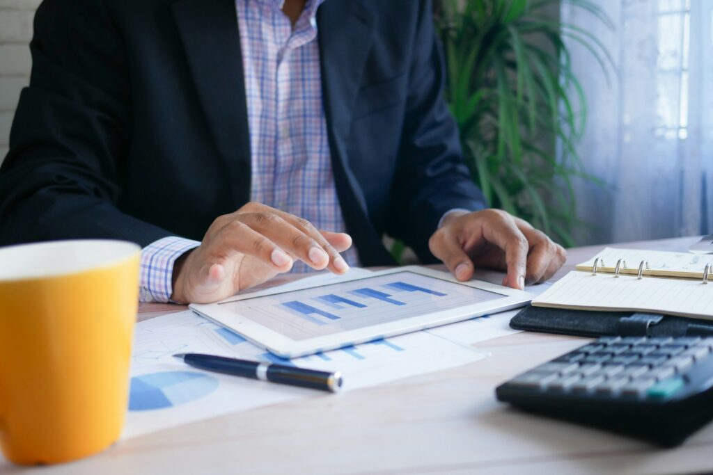 a man in a blue blazer and checked white shirt looks at the graphs in a white tablet on an office desk | Nextworld revenue system concept