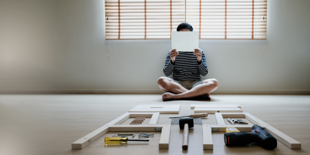 Person sitting on the floor reading instructions surrounded by tools, parts and pieces of wood | composable ERP.